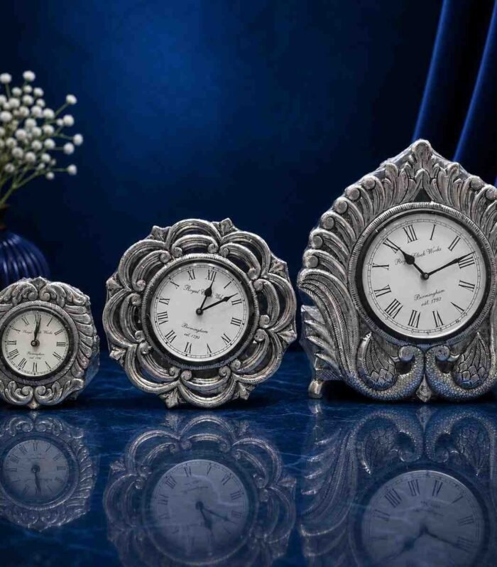 Set of three ornate 999 silver sheeting table clocks on a blue marble surface Gokulam Signature Jewels